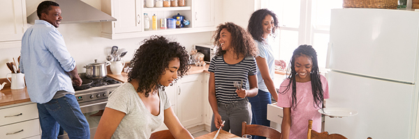 A family of five set the table and prepare dinner together in a bright kitchen.